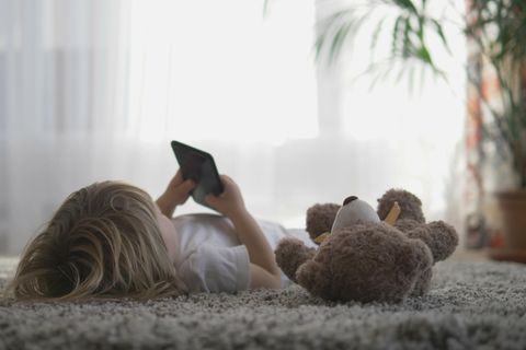 Wann hat Euer Kind ein eigenes Handy bekommen? Mädchen liegt mit Handy und Teddybär auf dem Boden