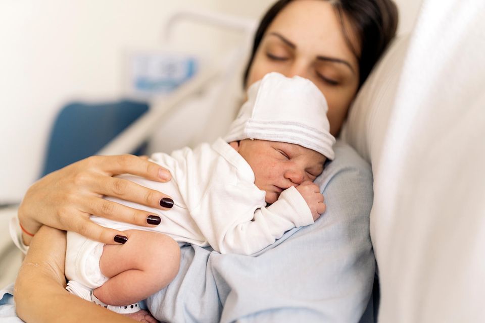 Labienriss (Schamlippenriss): Mutter kuschelt mit ihrem Neugeborenen im Krankenhausbett