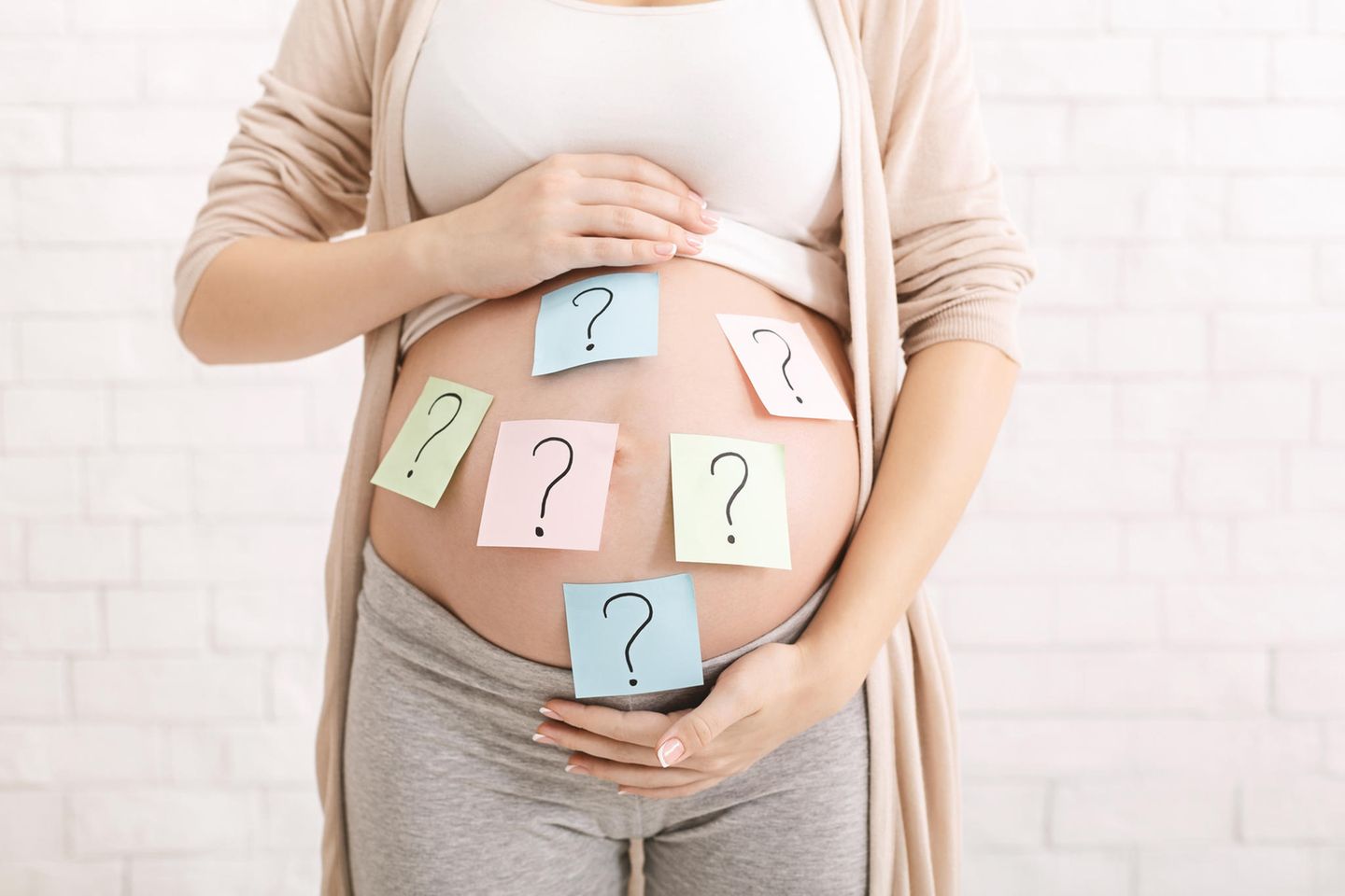 Ab wann lässt sich das Geschlecht erkennen? Schwangere Frau hat Zettel mit Fragezeichen auf ihren Bauch geklebt