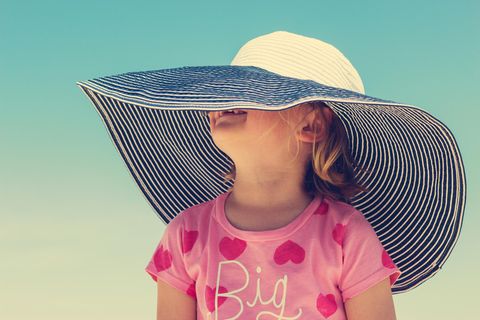 Sonnenallergie Kind: Kleines Mädchen im rosa T-Shirt unter einem riesigen Strohhut