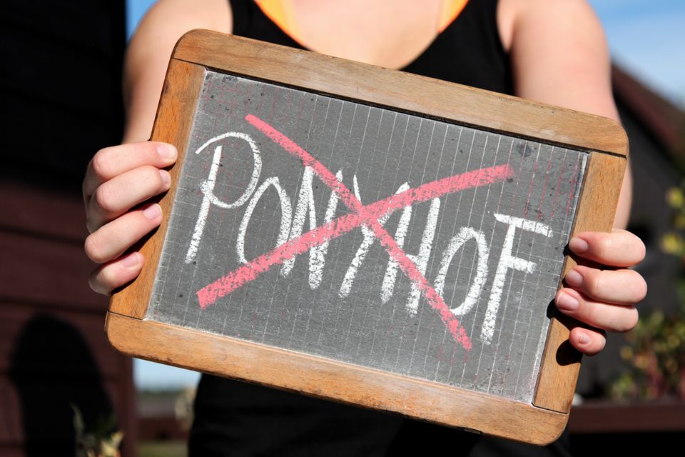 Frau hält Tafel mit dem durchgestrichenen Schriftzug "Ponyhof"