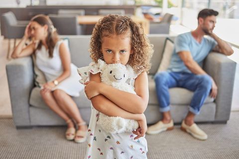 Trennung mit Kindern: Kind hält ein Kuscheltier im Arm und steht vor zwei Erwachsenen auf einem Sofa