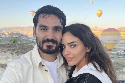 Ilkay und Sara Gündogan stehen vor einer Hügellandschaft mit Heißluftballons im Himmel