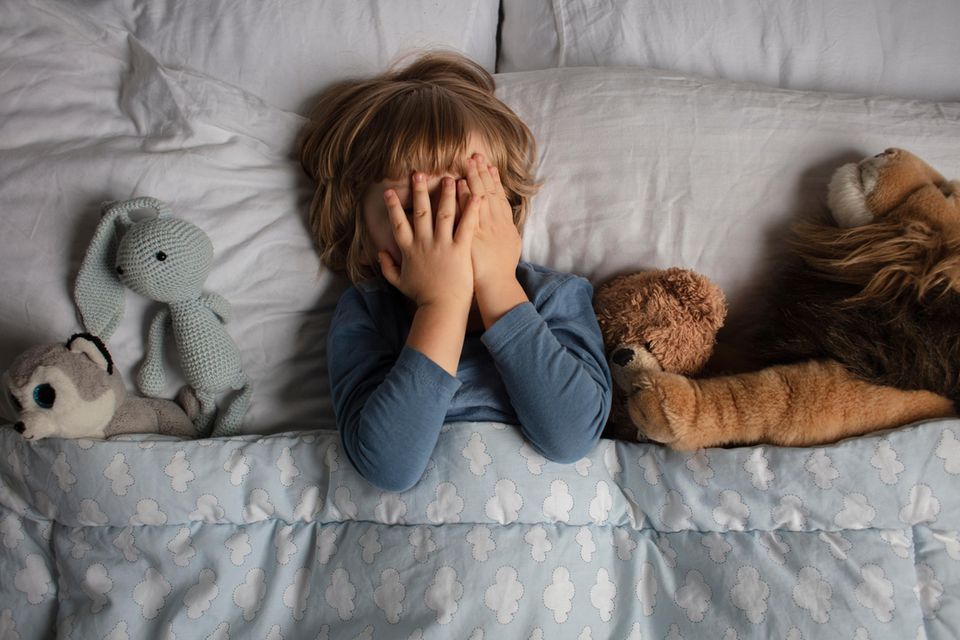 Nachtschreck bei Kindern: Kind liegt im Bett und verdeckt sein Gesicht mit den Händen