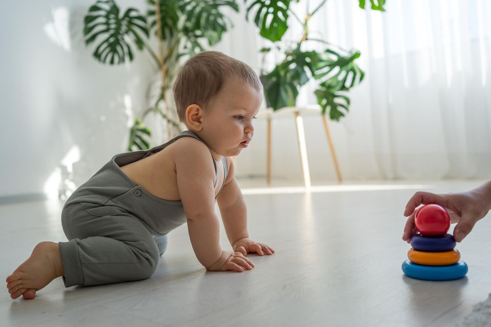 Spielzeug für 1-Jährige: Kleinkind krabbelt auf einen bunten Stapelturm zu.