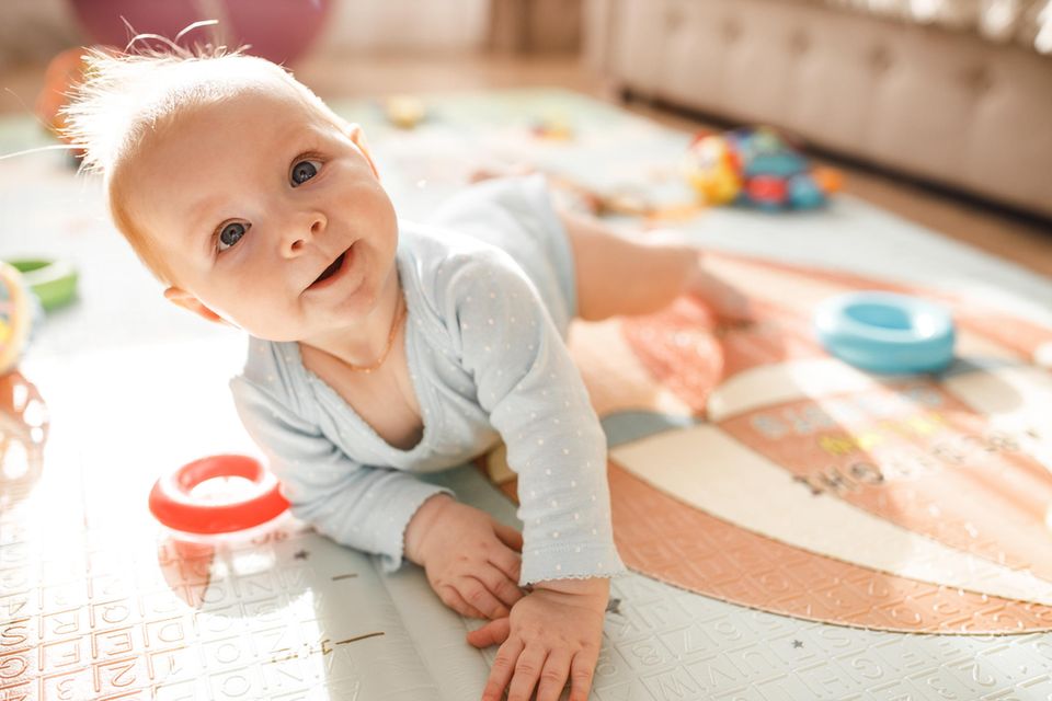 Allergien vorbeugen: Baby auf einem Spielteppich, schaut hoch