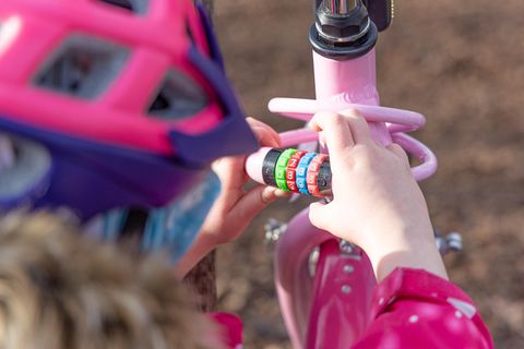 Fahrradschloss für Kinder im Test: Kind mit pinkem Helm dreht an einem rosa Zahlenschloss.