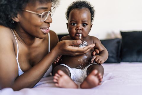 Speibaby: Schwarzes Baby spuckt Milch aus in die Hand der Mutter