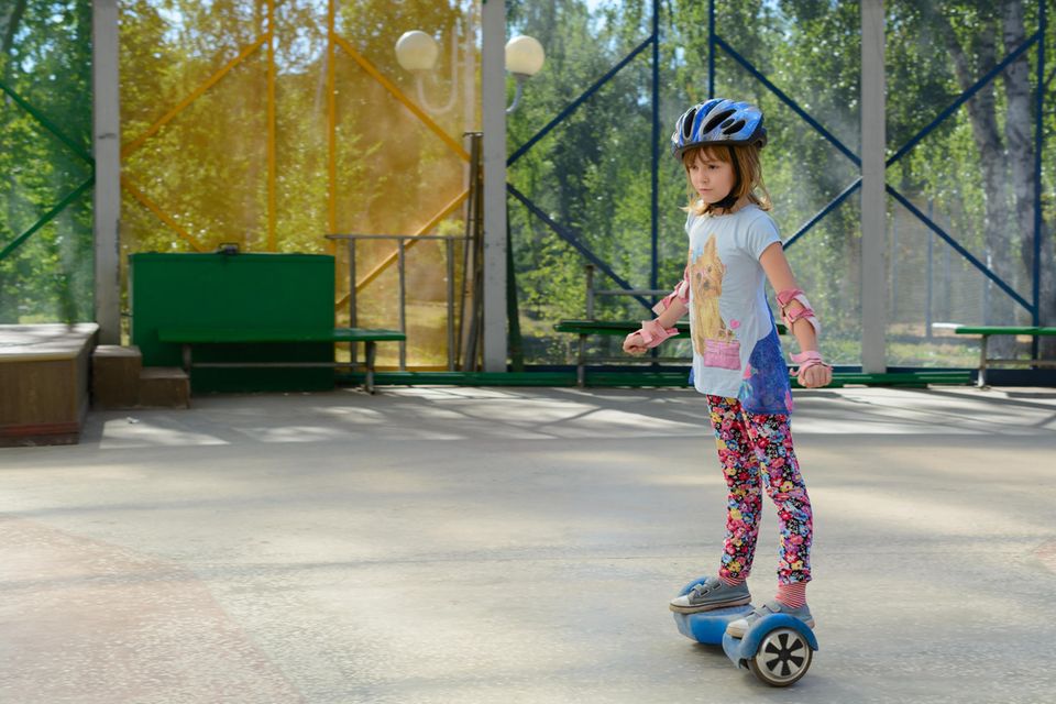 Hoverboards für Kinder im Test: Mädchen mit Helm und Schonern fährt auf Hoverboard