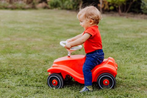 Rutschautos für Kinder: Mädchen fährt auf Bobby-Car durch den Garten