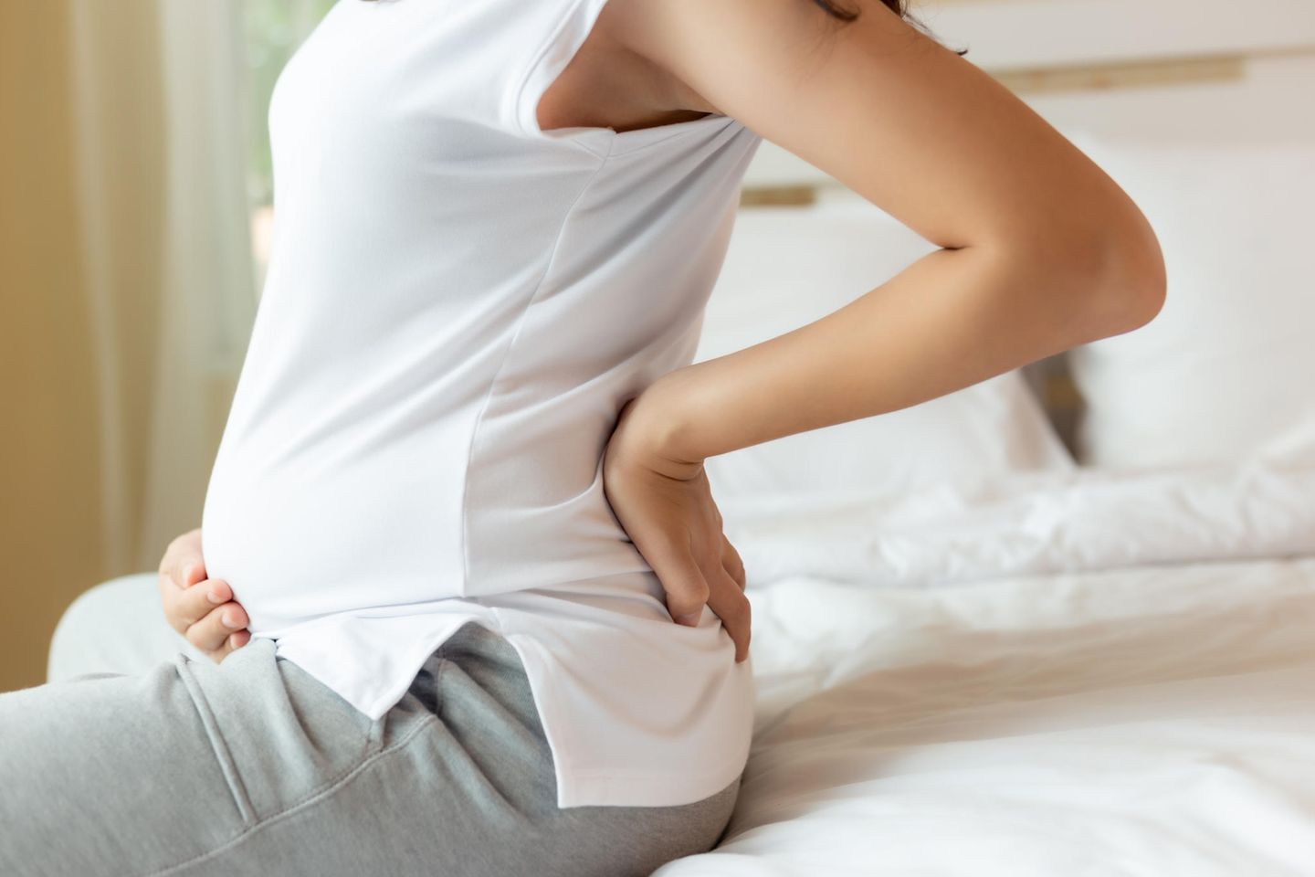 Hinterwandplazenta: Schwangere Person sitzt auf Bett und fasst sich an Bauch und Rücken