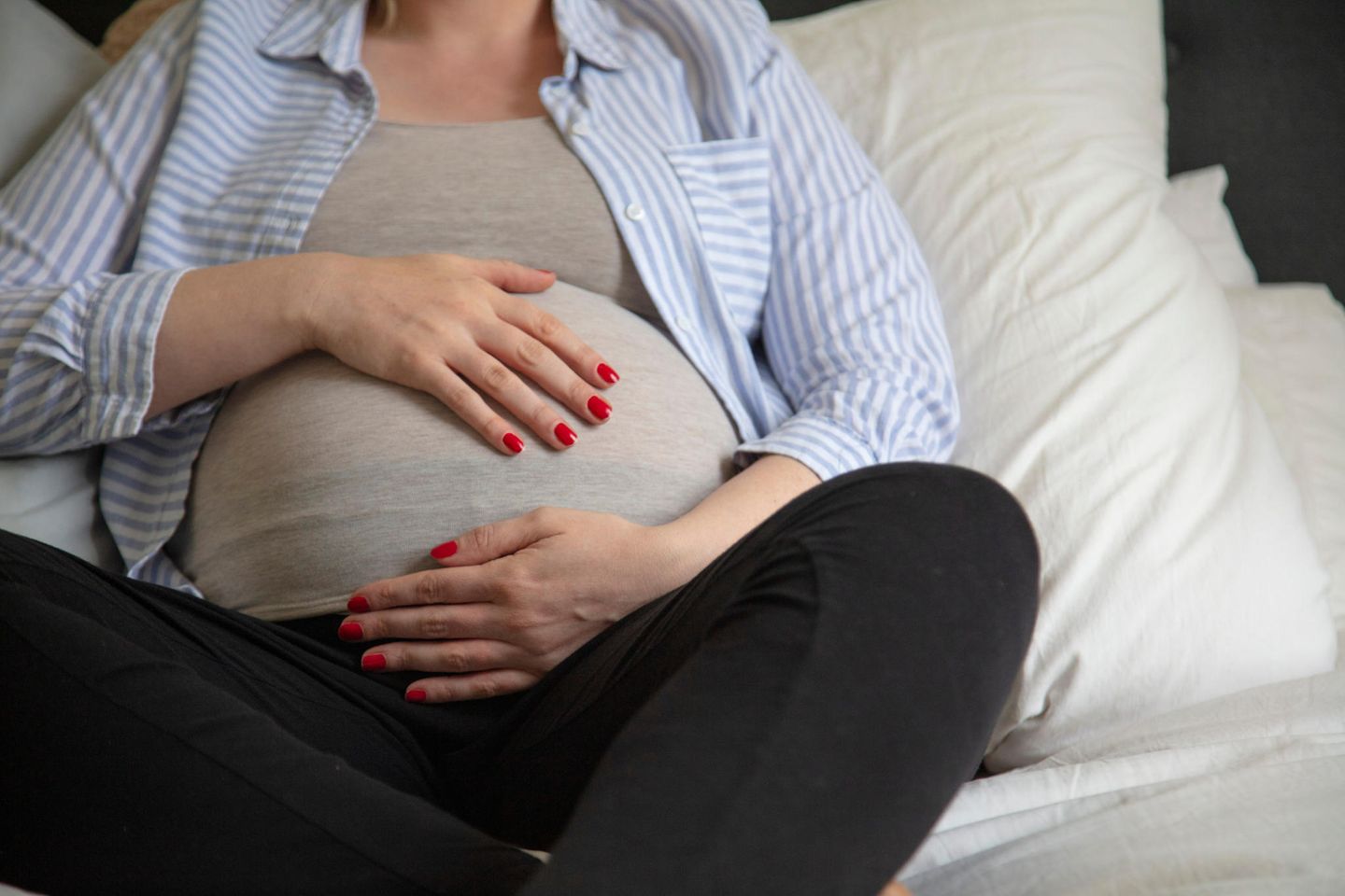 Plazenta praevia: Schwangere Person hält sich liegend mit beiden Händen den Bauch