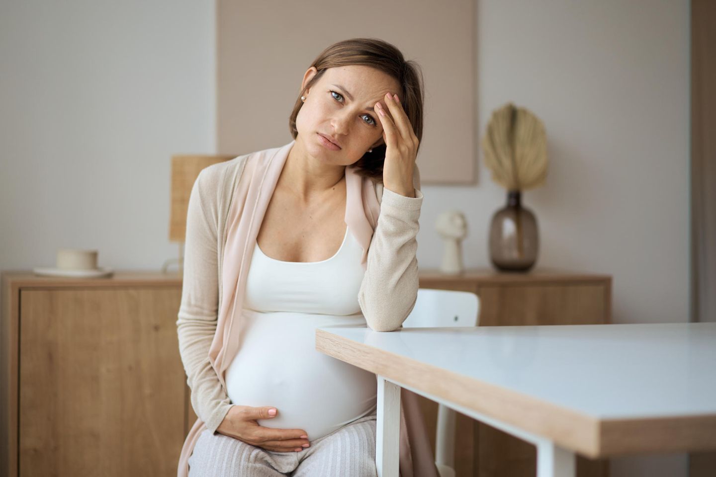 Plazentainsuffizienz: Schwangere sitzt auf einem Stuhl und schaut besorgt