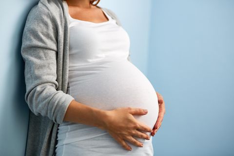 Verkalkte Plazenta: Schwangere steht an einer Wand und hält sich mit beiden Händen den Bauch