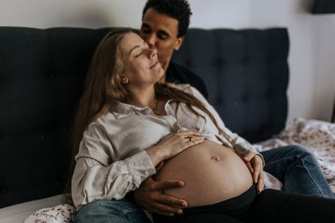 Schwangere entspannt in den Armen ihres Partners