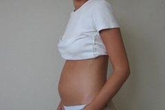 Frau hat weißes Tshirt hochgezogen und zeigt einen kleinen Babybauch.