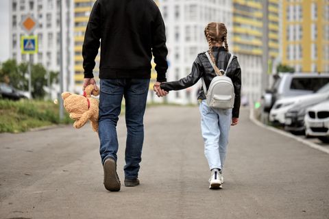 Mann geht mit Kind an der Hand einen Weg entlang