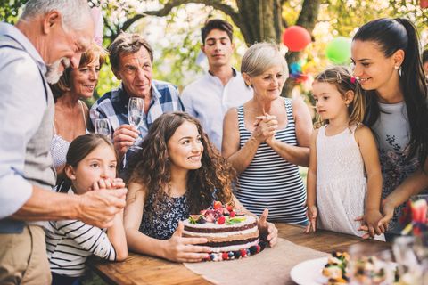 Jugendweihe-Geschenke: Lächelnde Jugendliche mit Kuchen am Tisch im Kreis der Familie