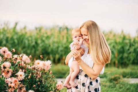 Glückliche Mutter mit Baby auf dem Arm am Blumenfeld