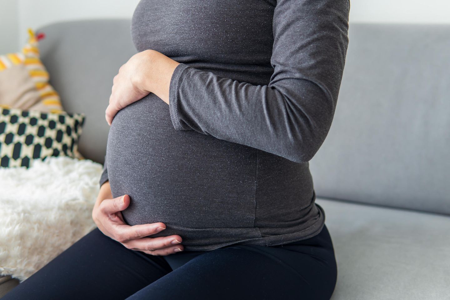 Plazentaablösung: Schwangere sitzt auf dem Sofa und hält sich den Bauch