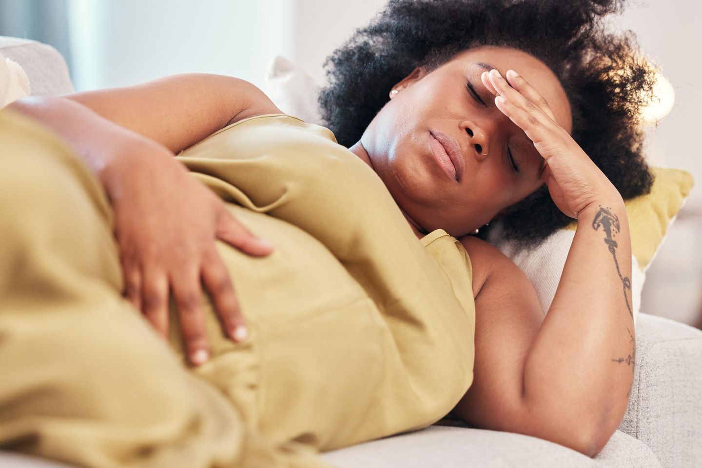 Blutungen in der Schwangerschaft: Schwangere Frau liegt auf dem Sofa und hält sich den Bauch