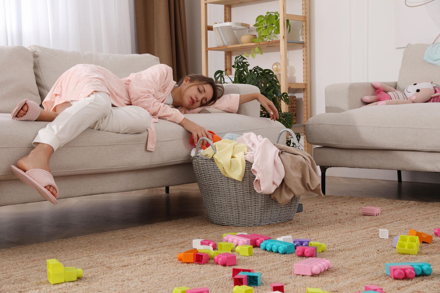 Mutter liegt geschafft auf dem Sofa im Chaos