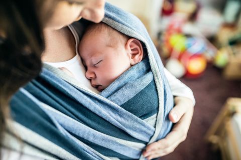 Tragetuch für Babys: Säugling schlummert im blauen Tragetuch an Mamas Brust.