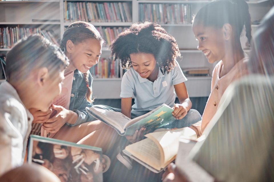 Die besten Kinderbücher: Lachende Kinder lesen gemeinsam in Bibliothek