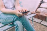 Mutmacher in der Kinderwunschzeit: Frau sitzt auf einer Bank und schaut auf ihr Smartphone