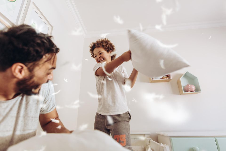 Vater und Sohn machen eine Kissenschlacht im Kinderzimmer