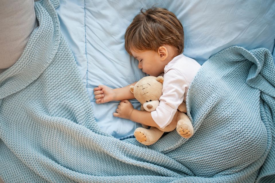 Schlafstörungen beim Kind: Ein kleiner Junge schläft mit Teddy Bär