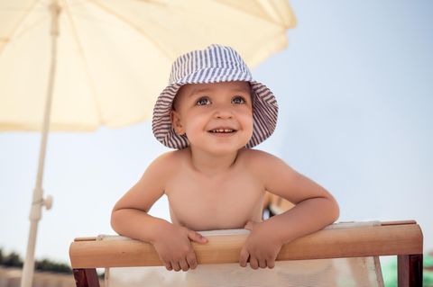 Sonnenstich bei Kindern: Kind mit Sonnenhut unter einem Sonnenschirm