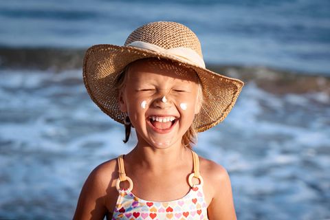 Sonnencremeflecken entfernen: Mädchen mit Strohhut und Sonnencreme im Gesicht lacht