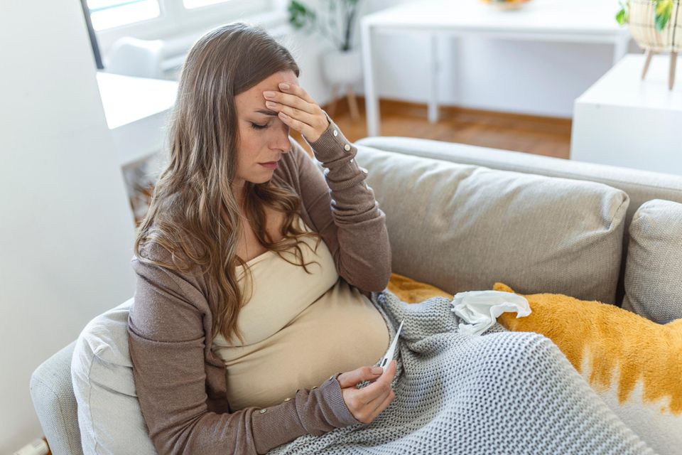 Windpocken in der Schwangerschaft: Schwangere schaut auf Fieberthermometer