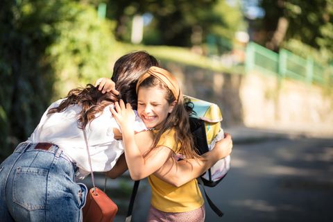 Mädchen mit Schulranzen umarmt draußen freudig ihre Mutter