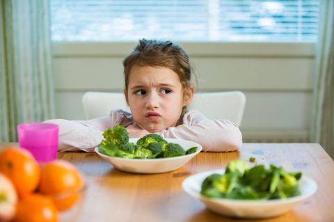 Eltern-Mythen: Ein Mädchen sitzt skeptisch vor einem Teller mit Gemüse