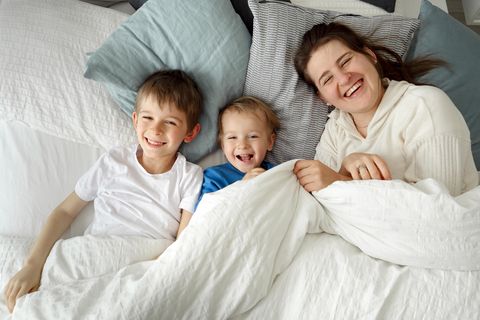 Lachende Mutter im Bett mit zwei Kindern