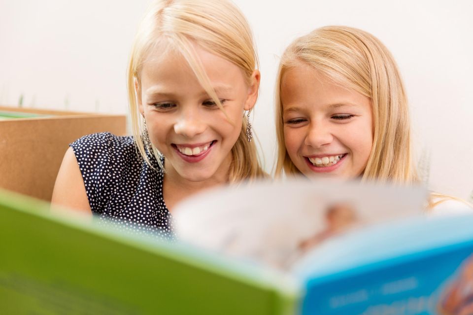 Zwei Mädchen blättern fröhlich in einem Buch