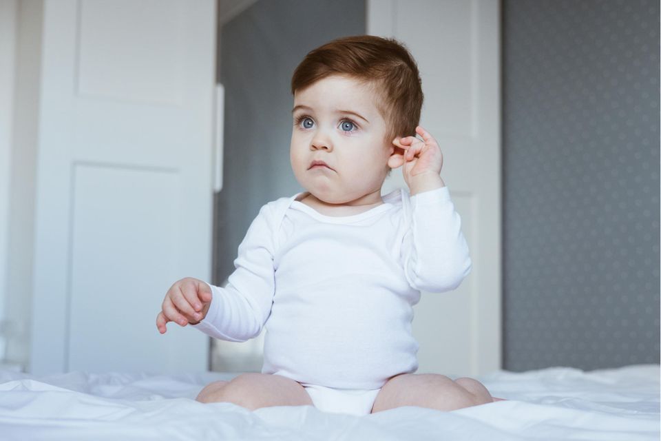 Mittelohrentzündung beim Kind: Babs sitzt auf einem Bett und greift sich ans Ohr