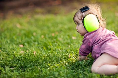 Gehörschutz für Babys: Kleinkind mit grünem Kapselgehörschutz krabbelt über Wiese.