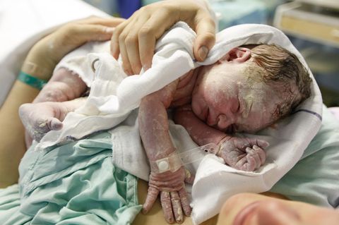 Neugeborenes mit Käseschmiere liegt nach der Geburt auf dem Bauch der Mutter