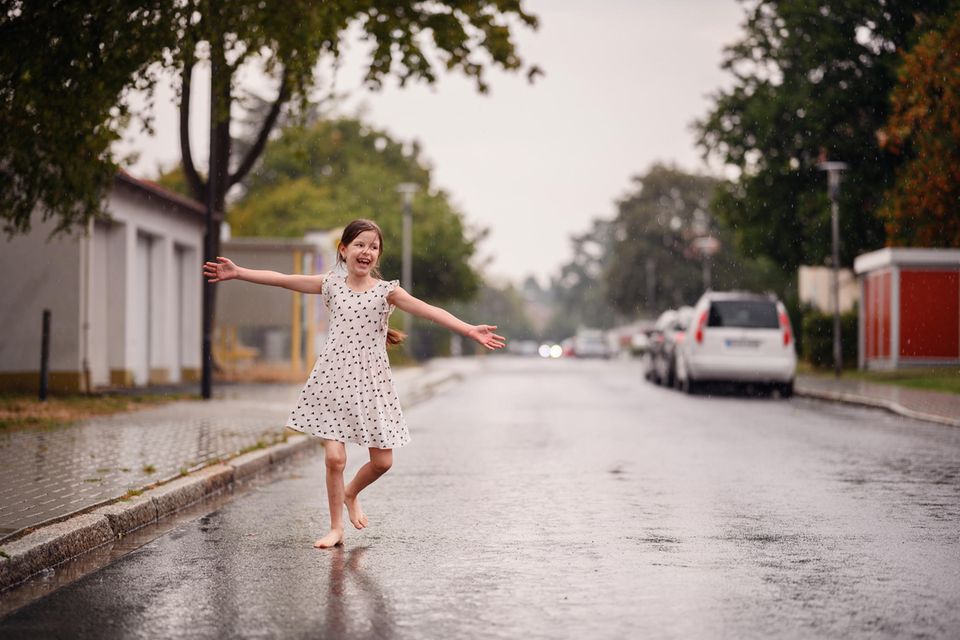 Laissez-faire-Erziehungsstil: Mädchen tanzt barfuß auf regennasser Straße