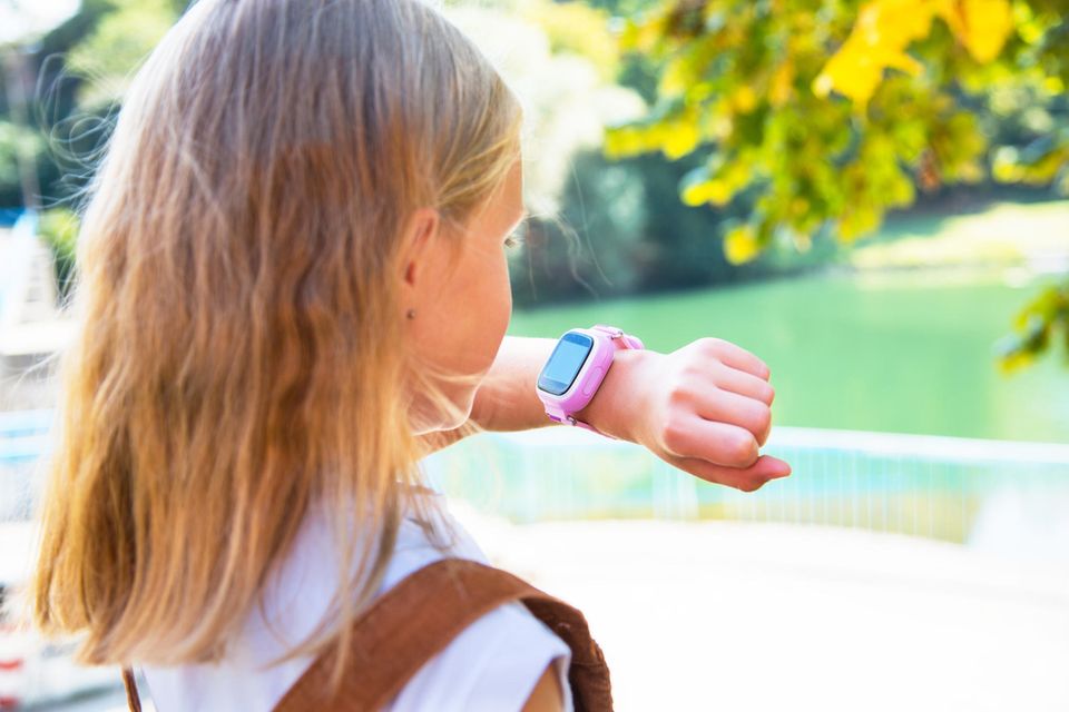 Mädchen schaut auf die rosa Smartwatch an ihrem Handgelenk.