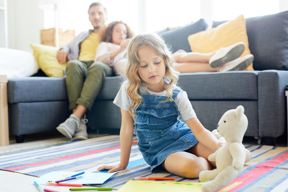Lazy Parenting im Praxistest: Kind spielt auf dem Boden, Erwachsene sitzen auf einem Sofa