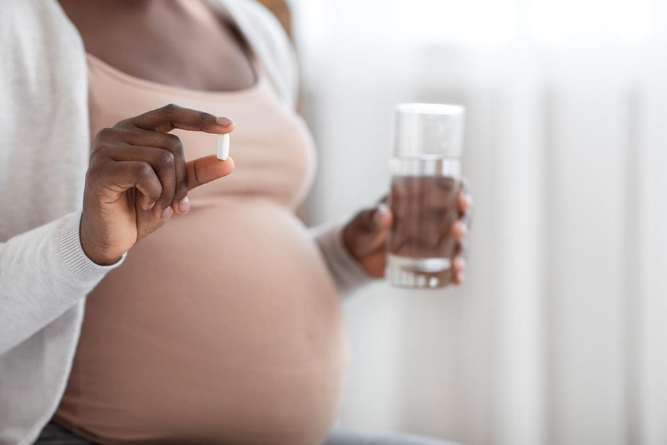 Antibiotika in der Schwangerschaft: Schwangere schwarze Frau hält Tablette und Wasserglas in den Händen