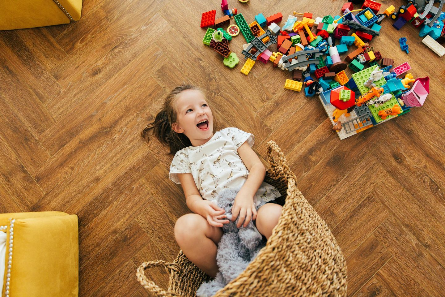 Lego Aufbewahrung Ideen: Fröhliches Mädchen liegt neben einem Haufen Lego mit einem Korb auf dem Boden.