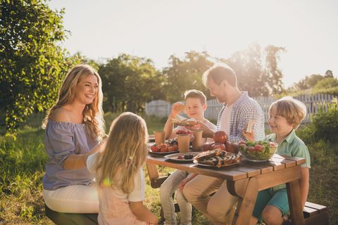 Spätsommerküche: Familie sitzt am Tisch im Garten und isst