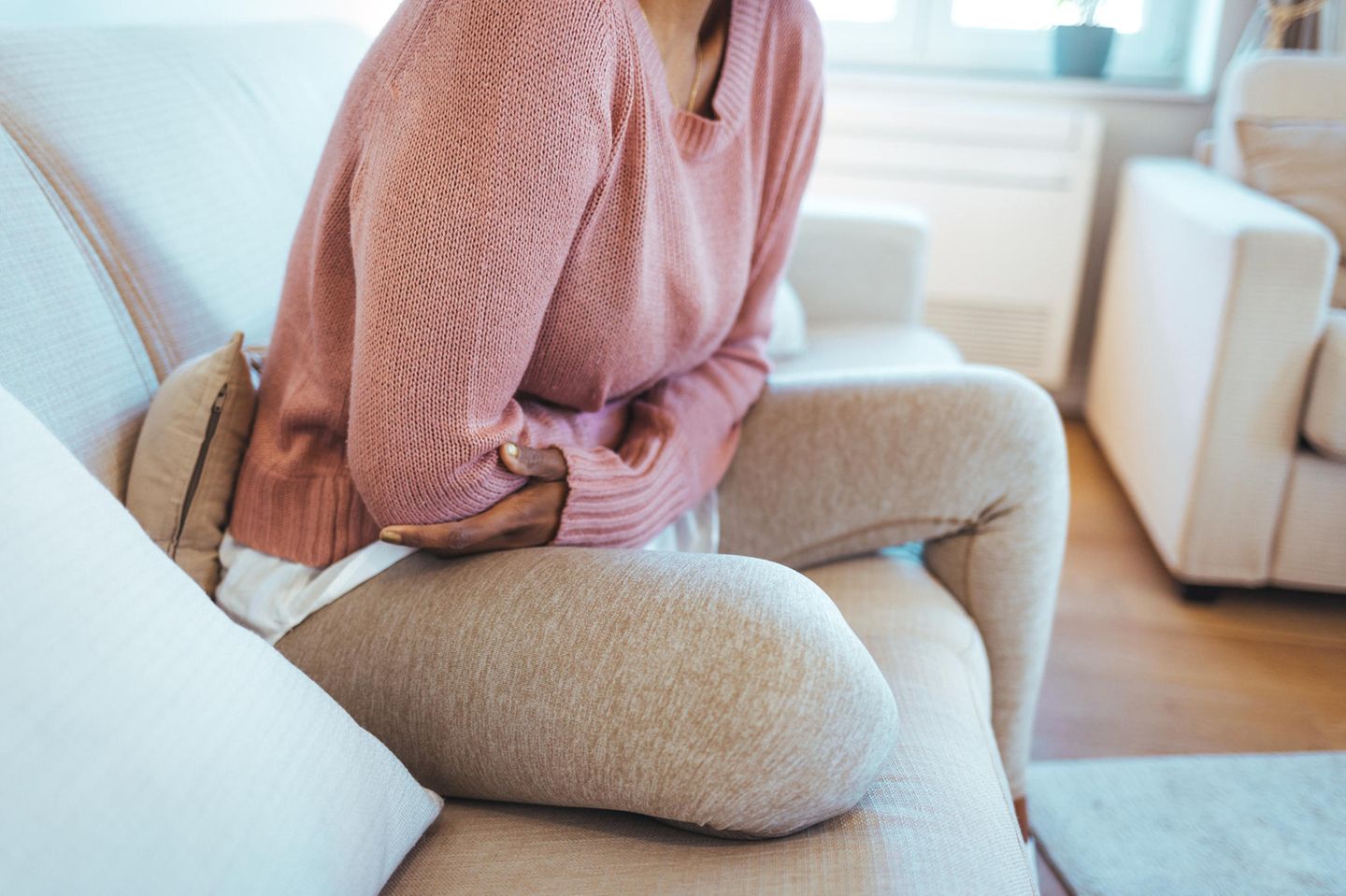 Eisprungsymptome: Frau in rosa Pulli und Leggings hält sich den Unterleib