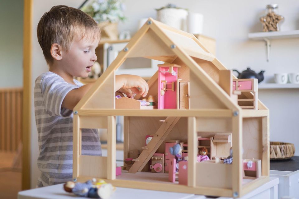Puppenhaus im Kinderzimmer: Junge spielt mti Puppenstube auf dem Tisch.