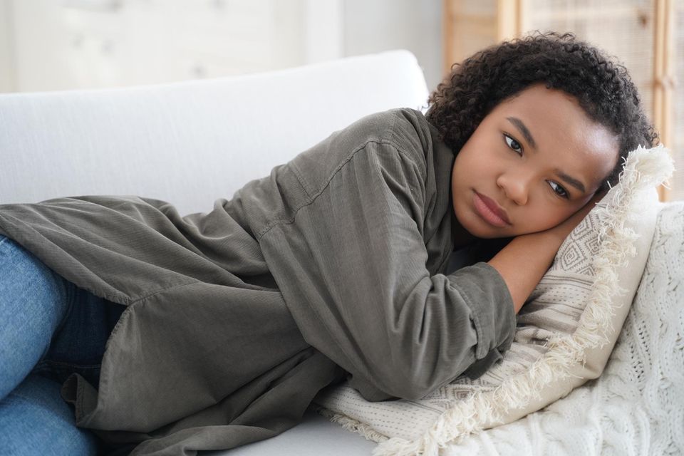 Erste Regel: Mädchen liegt mit Unterleibsschmerzen auf Couch